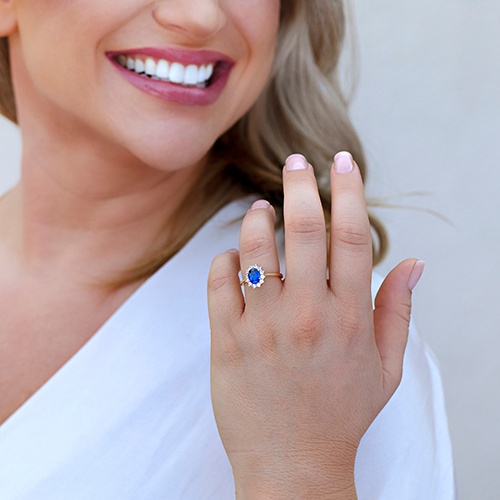 A woman smiles while wearing a royal-inspired oval sapphire engagement ring with white gemstones. 